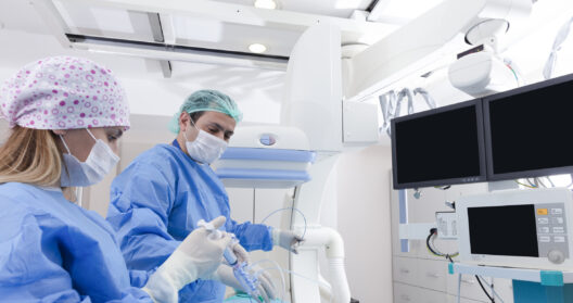 Two surgeons in scrubs and masks working together in a hospital operating room during a cryoablation surgical procedure.