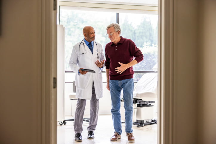 Male doctor talking with senior man in exam room experiencing symptoms after the mesothelioma latency period