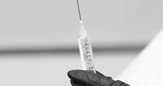 A black-gloved hand holds a syringe in a sterile setting, emphasizing medical precision.