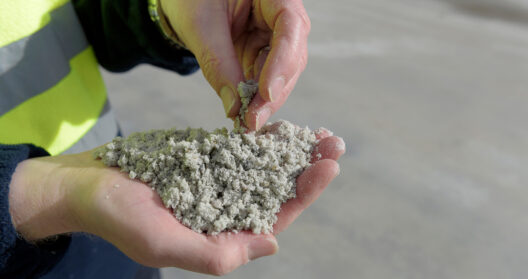 Close up of workers hands in a high-visibility jacket examining a handful of sand.